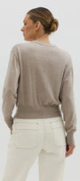 Woman wearing a beige sweater and white pants on a plain background
