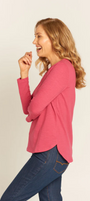 Woman wearing a pink long-sleeve top and blue jeans on a beige background