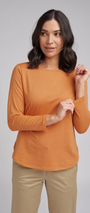 Woman wearing an orange long-sleeve top and beige pants against a gray background