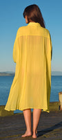 Woman in a yellow dress standing on a dock with a blue sky and water background