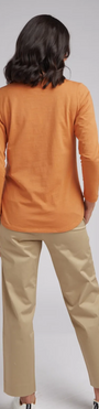 Woman wearing an orange top and beige pants on a gray background