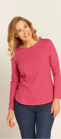 Woman wearing a pink long-sleeve top and blue jeans on a light background