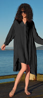 Woman in a black dress standing on a wooden dock by a body of water.
