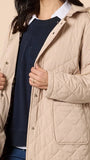 Person wearing a beige quilted coat over a navy sweater with a logo on a beige background