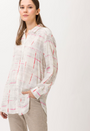 A female model wearing a beige long sleeved shirt with pink and white geometric pattern.