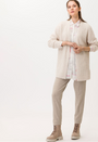 A female model wearing a beige long sleeved shirt with pink and white geometric pattern.