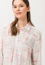 A female model wearing a beige long sleeved shirt with pink and white geometric pattern.