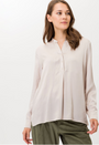 A woman wearing a beige velvet longsleeve shirt with a straight neckline and a button placket in the front.