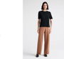 A person wearing a black short sleeve knit top and brown pants, standing against a white background.